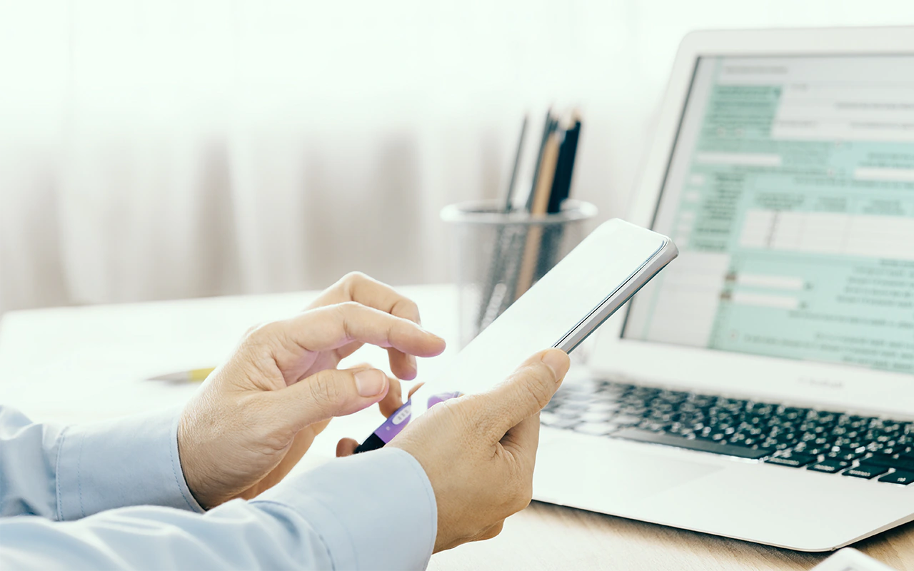 person holding phone in front of computer